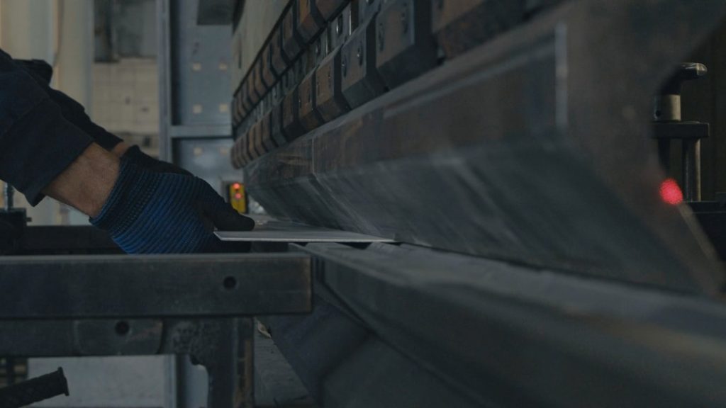 A workers gloved hands carefully position a metal sheet in a press brake machine, ensuring precision in the bending process. The image highlights craftsmanship and industrial technology.