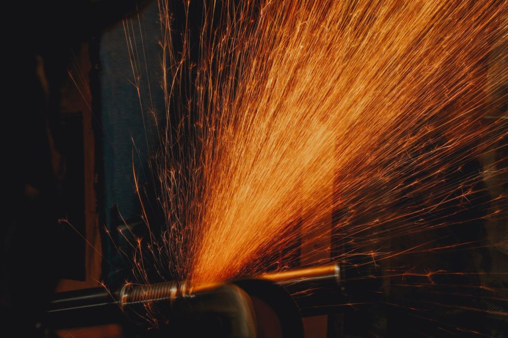 Dramatic close-up of vibrant orange sparks flying from a grinding machine, illuminating a workshop setting.