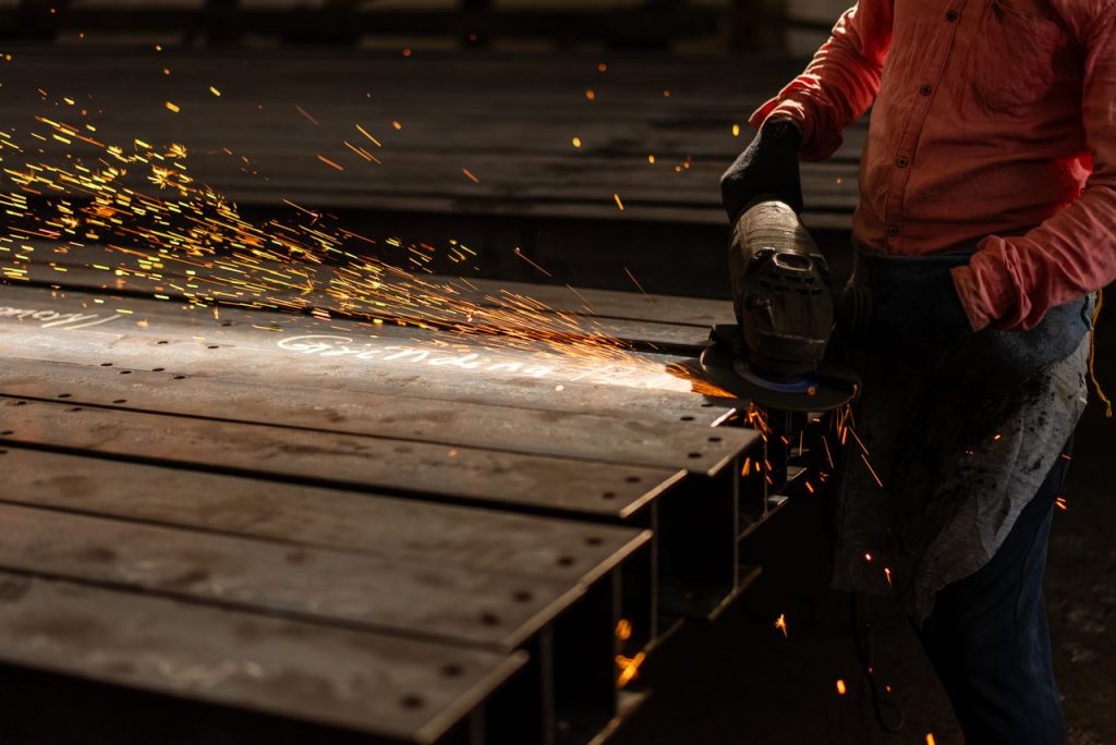 A worker grinds metal beams with an angle grinder, creating vibrant sparks in an industrial setting.